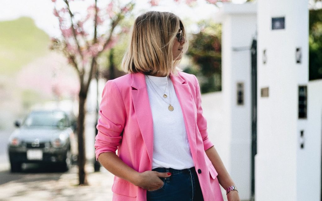 Žena u modernom ružičastom sakou, bijeloj majici i farmerkama na osunčanoj ulici – proljetni stajling