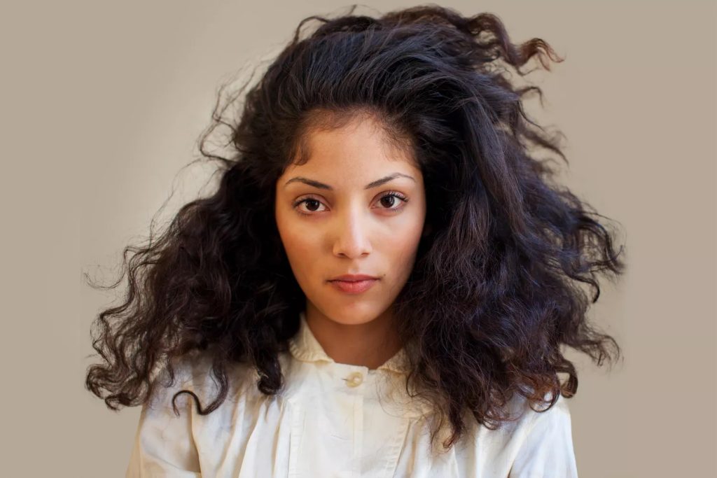 Krupni kadar žene sa izuzetno gustom, prirodnom i voluminoznom tamnom kovrdžavom kosom, koja ilustruje potencijal za bujniju kosu uz pravilnu njegu.