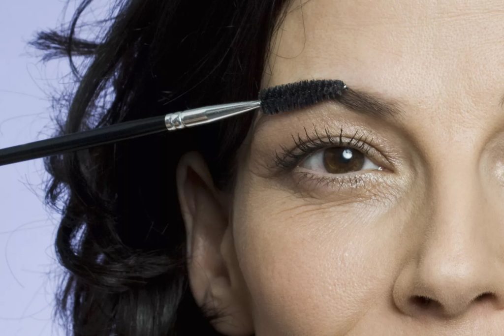 Žena iznad 50 godina oblikuje obrve četkicom za svjež izgled lica.