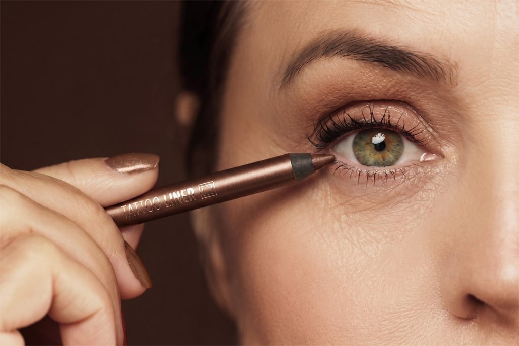 Žena preko 50 godina pokazuje kako se pravilno nanosi ajlajner. Krupni kadar oka sa blagom šminkom koja ne naglašava bore i vizuelno otvara pogled.