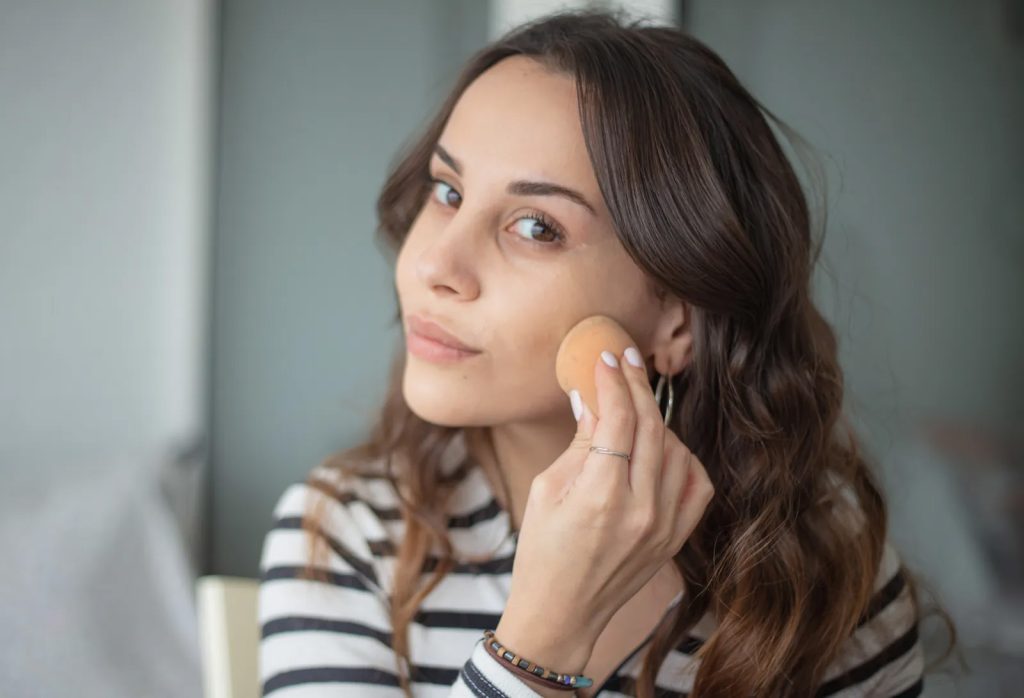 Žena nanosi puder na lice spužvicom kako bi provjerila da li se nijansa stapa sa kožom