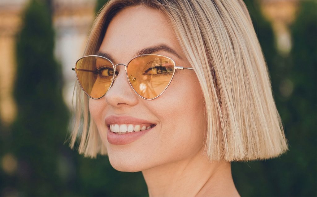 Nasmijana žena sa modernom plavom paž frizurom i sjajnom dlakom nakon pravilne njege kose.