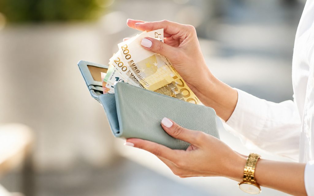 Žena vadi novčanice iz novčanika, simbol finansijske sigurnosti i novčanog dobitka.