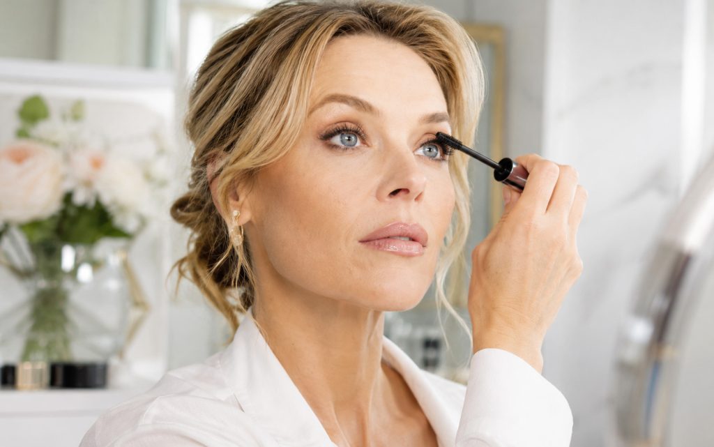 Žena u četrdesetim godinama nanosi maskaru u elegantnom i svijetlom beauty ambijentu.
